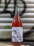 Rosé sparkling wine bottle with an illustrated label featuring a playful horse and sun motif, set against a metallic shutter with graffiti accents in an urban Berlin setting.
