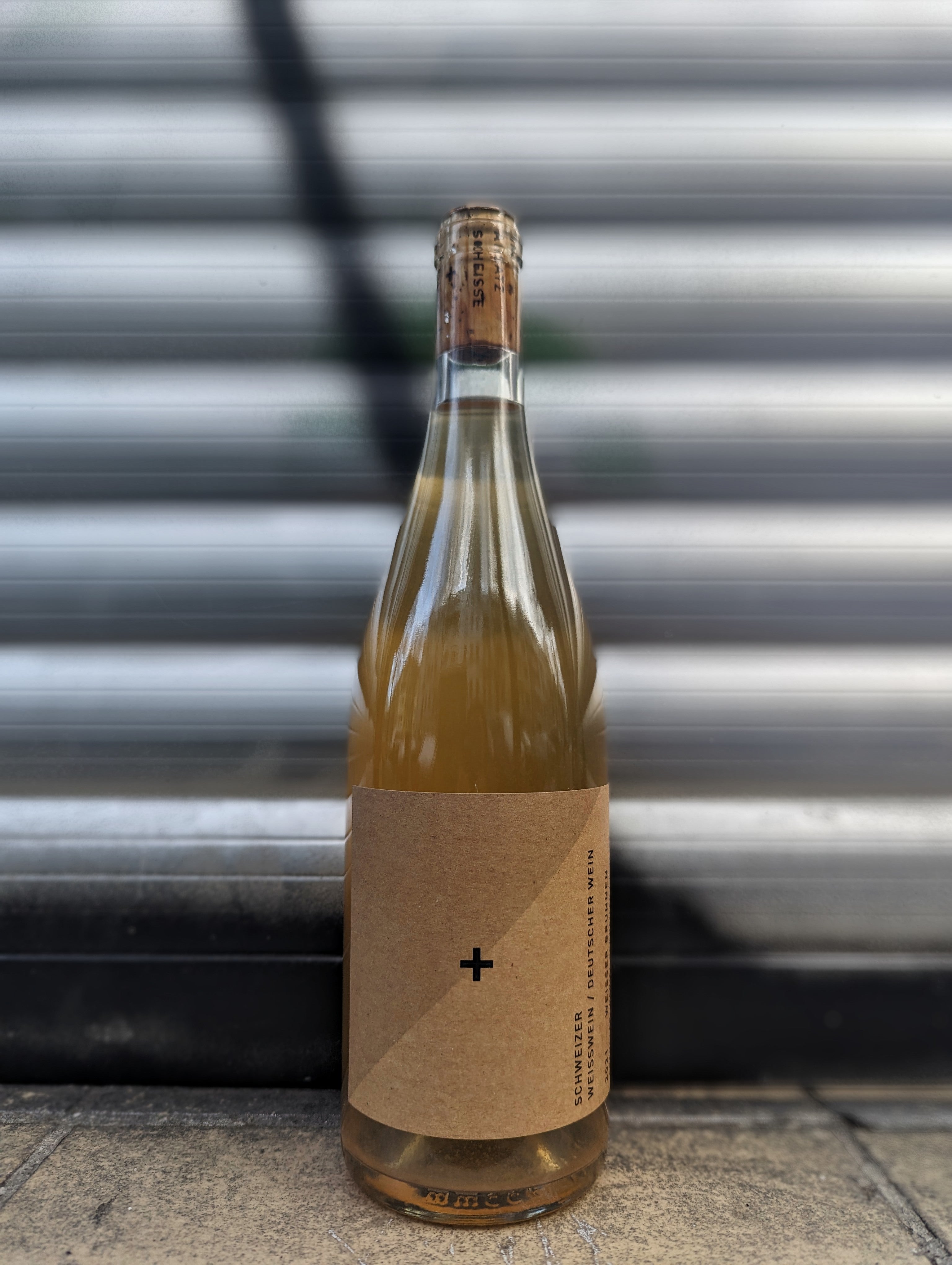 White wine bottle with minimalist kraft paper label  set against a metallic shutter with graffiti accents in an urban Berlin setting.