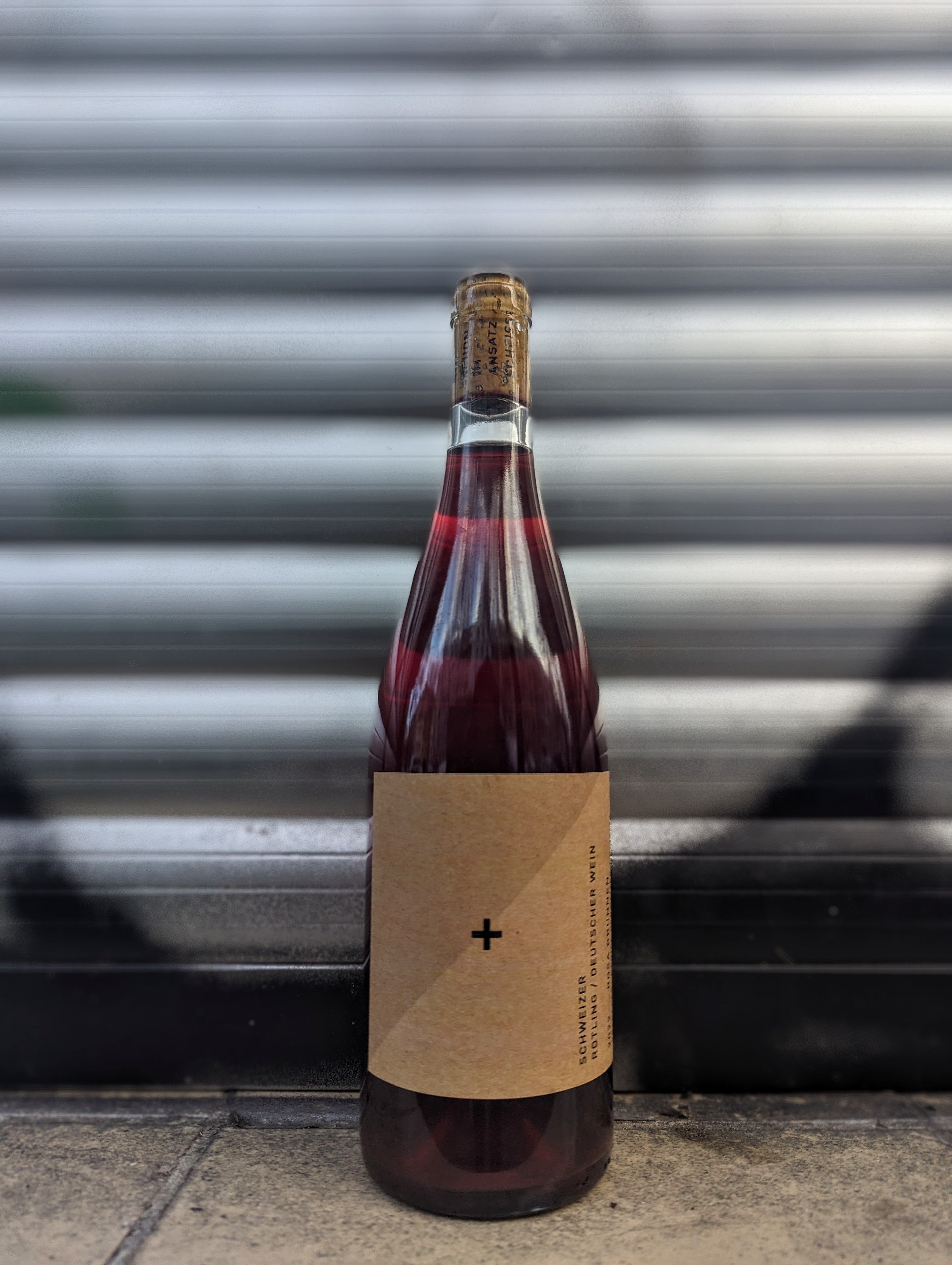 Rosé wine bottle with a minimalist kraft paper label set against a metallic shutter with graffiti accents in an urban Berlin setting.