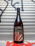 Dark glass wine bottle with a beige and red label displaying the bold black text "ROTER REBELL 2023." The label features a red raised fist graphic over radiating stripes. The bottle is set against a metallic, graffiti-covered background with a red paint splatter on the ground.





