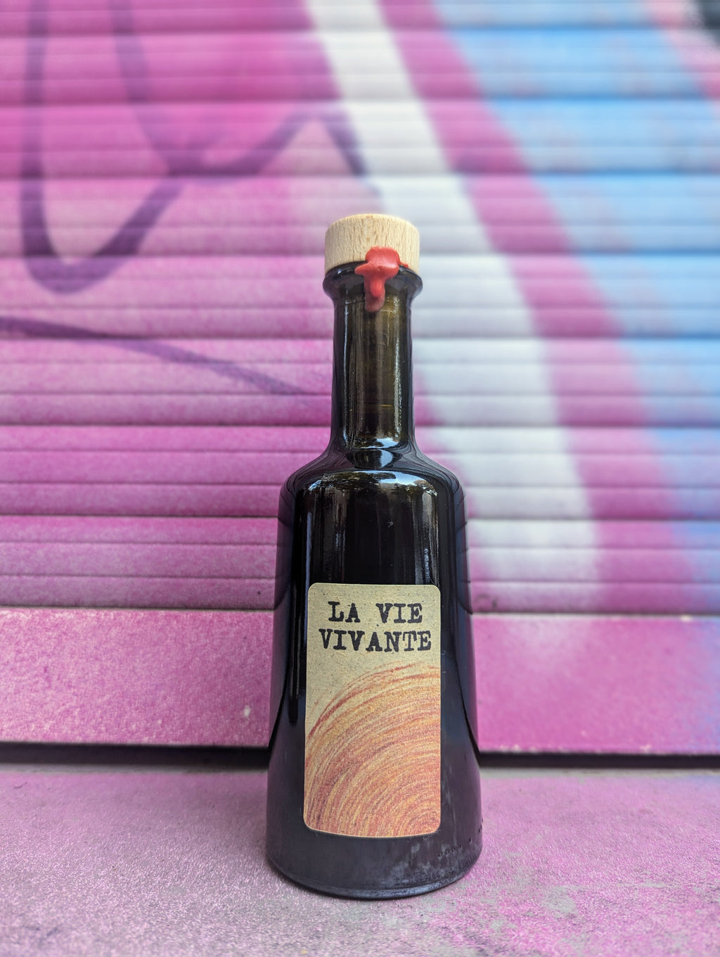 Vinegar bottle called a vie vivante with a minimalist kraft paper label set against a colorful graffiti-covered shutter in an urban Berlin setting.