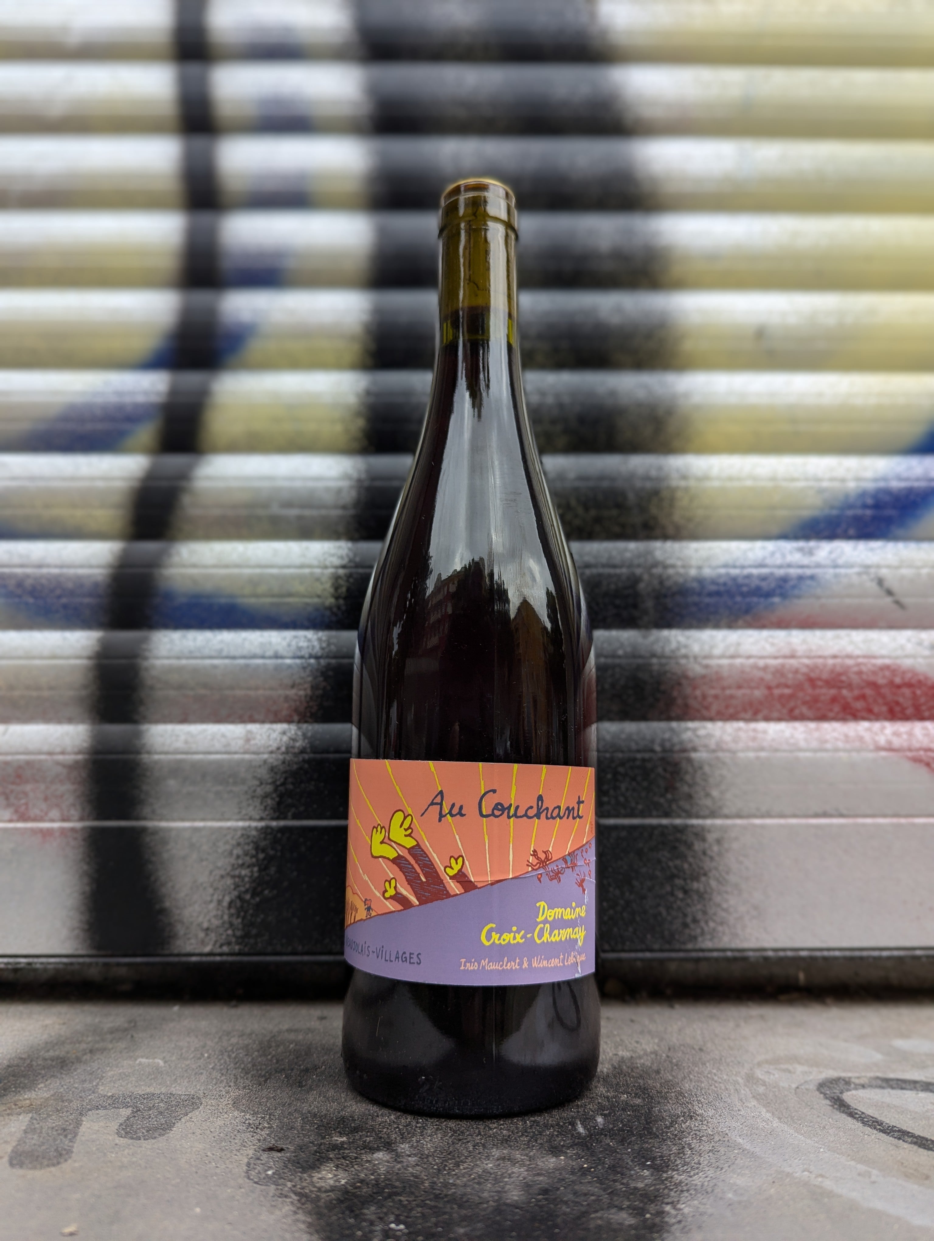 Red natural wine bottle set against a graffiti-covered shutter in an urban Berlin setting.