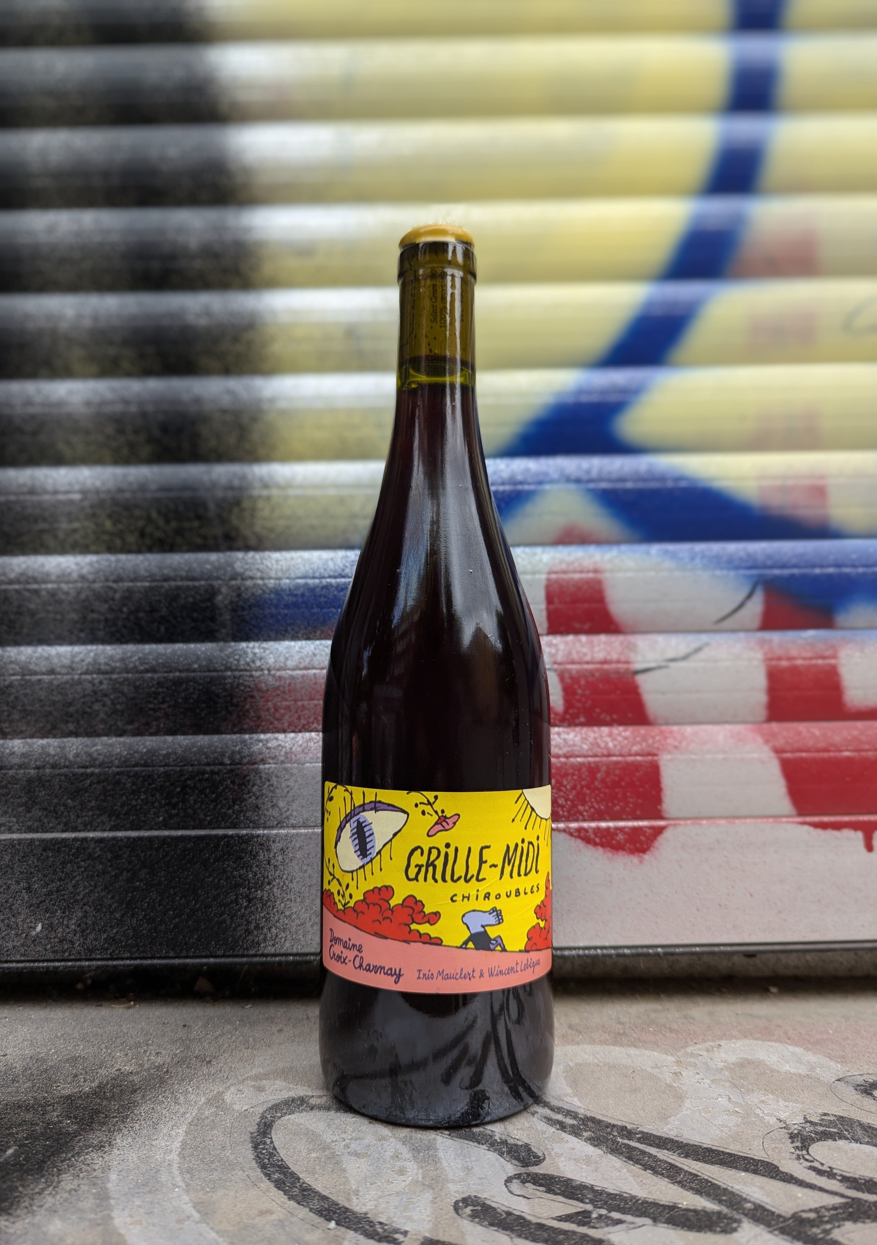 Grille-Midi natural wine bottle with a colorful label, set against a graffiti-covered shutter in an urban Berlin setting.