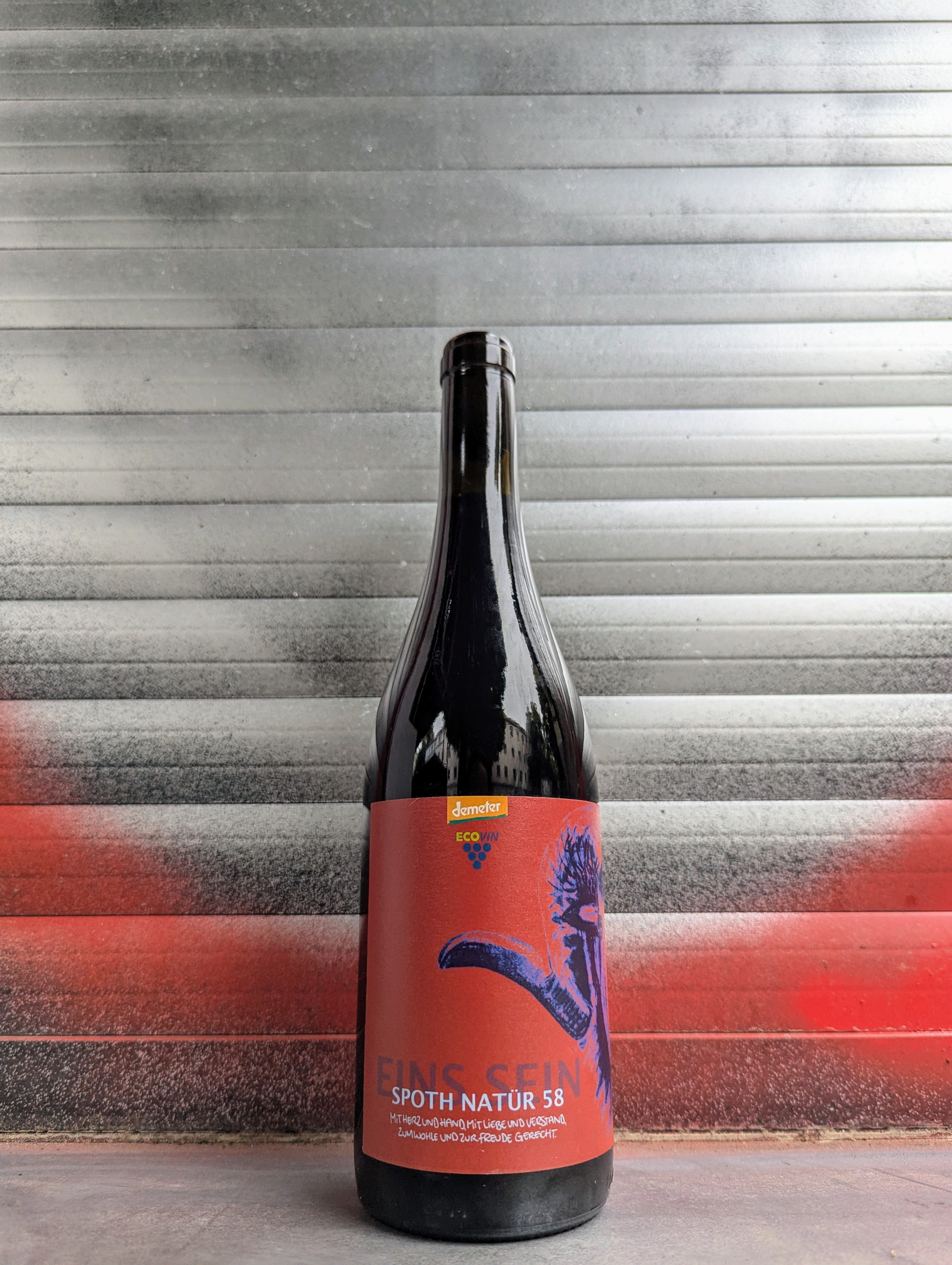 Bottle of Spoth Natur 58 natural wine with a bold red label featuring blue artistic graphics, set against a metallic background with red and black graffiti.